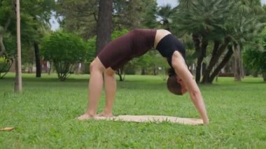Yoga pozu veren kadın, köprü ve arka eğri şeklinde yükselen yay ile, yemyeşil parkta etkileyici esneklik ve denge sergiliyor.