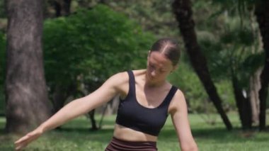 Spor hocası, yoga pozunun çeşitliliğini gösteriyor. Kollarını paspasın üzerinde sallıyor. Huzur parkı ortamında yemyeşil, sağlık ve refahı teşvik ediyor.