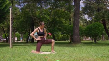 Spor hocası, parkta yan hamleler yaparken, doğa tarafından çevrelenmiş olan sakin doğa ortamında tekniğin ve hareketin altını çizerek, uygun şekli sergiliyor.