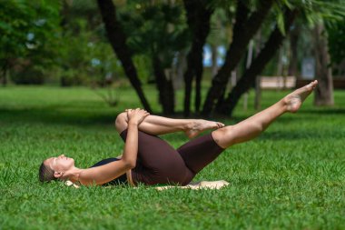 Spor elbiseli genç bir kadın parkta çimlerin üzerinde uzanan bir paspasın üzerinde egzersiz yapıyor. Kadın zihinsel ve fiziksel sağlığıyla ilgilenir. Akıllı Fitness, Esneme, Yoga