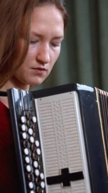 Kırmızı kazaklı genç bayan müzisyen son derece etkileyici taklit heyecanıyla akordeon çalıyor, profesyonel teknikle melodiyi seslendirirken müzik tutkusunu yakalıyor. dikey video