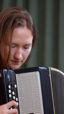 Kırmızı kazaklı genç bayan müzisyen son derece etkileyici taklit heyecanıyla akordeon çalıyor, profesyonel teknikle melodiyi seslendirirken müzik tutkusunu yakalıyor. dikey video