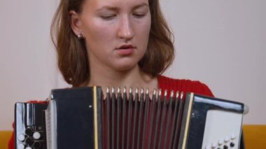 Kırmızı kazak giyen genç bayan müzisyen çok anlamlı yüz duygularıyla akordeon çalıyor, müzikal tutkuları yakalıyor ve yetenekli profesyonel tekniklerle karışık melodiler çalıyor..