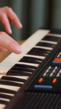 Kırsal ahşap masaya yerleştirilmiş elektronik klavye çalarken melodik kompozisyon yaratan kadın sanatçı, rahat ev ortamında müzikal tutkuyu ifade ediyor. dikey video