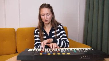 Kadın müzisyen elektronik klavyede yeni şarkı çalışıyor, parmaklar ev stüdyosunun tuşlarında ahşap masa ile hareket ediyor, müzik yaratıcılığı ve tutkusunu yakalıyor.