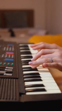 Kadın besteci kompleks elektronik klavyede melodik sesler yaratırken rahat rahat rahat ev ortamındaki parlak sarı kanepede oturuyor. dikey video