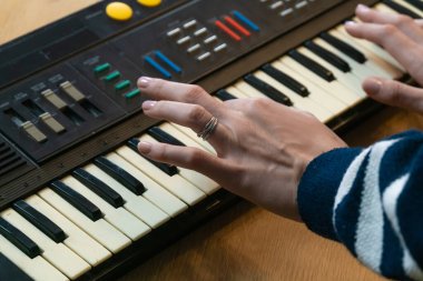 Ahşap bir masada klasik bir sentezleyici klavyesini ustalıkla çalan eller nostaljinin özünü yakalıyor ve rahat bir ev stüdyosunda müzik yaratıcılığı yaratıyor.