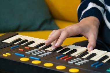 Kadın müzisyen sarı bir kanepede klasik bir sentezleyici çalıyor. Samimi bir ev stüdyosunda tutku ve beceriyle elektronik müzik yaratıyor.