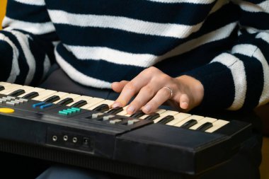 Bir müzisyenin elinin, klasik bir sentezleyiciyi ustalıkla çalarken, rahat bir ev stüdyosunda elektronik müzik yaparken, şık çizgili bir süveter giyerken yakın plan görüntüsü.