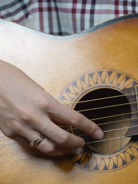 Bir müzisyenin elinin akustik gitarı ustaca çalarken, telleri tutkulu bir şekilde çekerken ve duygu ve sanatla yankılanan güzel melodiler yaratırken yakın plan görüntüsü. Dikey fotoğraf