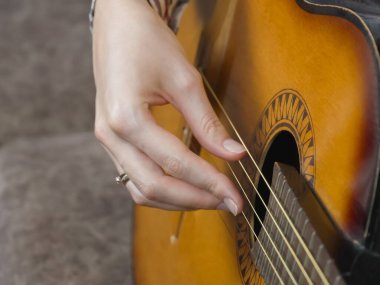 Bir müzisyenin elinin yakın plan çekimi, akustik gitar tellerinin ayarlarını hassas bir şekilde ayarlamak, en iyi ses kalitesi için hassas bir perde ve rezonans sağlamak,