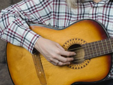 Akustik gitar çalan bir kadının ellerini yakından çekerek, müziğe olan derin tutkusunu ve enstrümanın işçiliğinin karmaşık güzelliğini vurguluyor.