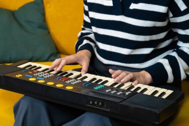 Kadın müzisyen sarı bir kanepede klasik bir sentezleyici çalıyor. Samimi bir ev stüdyosunda tutku ve beceriyle elektronik müzik yaratıyor.