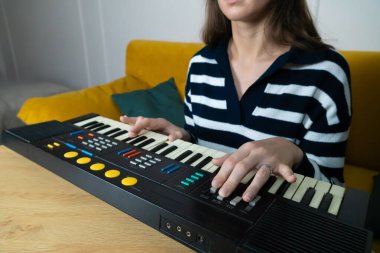 Ahşap bir masada klasik bir sentezleyici klavyesini tutkuyla çalan bir müzisyenin yakın çekimi melodik sesler ve ritimler yaratma sanatını vurguluyor.