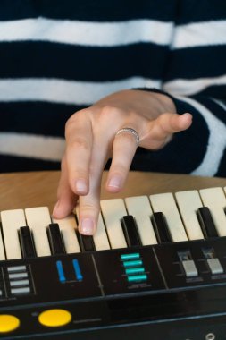 Klasik bir klavye sentezleyicisini ustalıkla çalan ellerin yakın plan görüntüsü, bir stüdyo ortamında ilgi çekici bir müzikal performans sırasında karmaşık elektronik sesler ve melodiler yaratıyor.