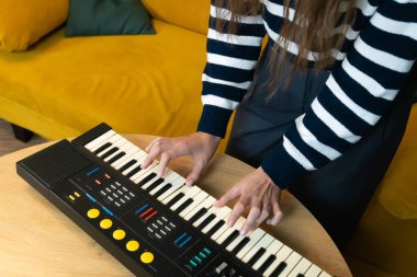 Ahşap bir masada taşınabilir bir sentezleyici klavye çalarken yakın plan çekimleri neşeli ve müzikal bir atmosfer yaratıyor.