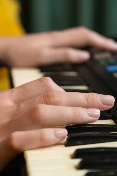 Kadın elleri ustalıkla klasik bir sentezleyici klavye çalıyor, rahat bir stüdyoda elektronik müzik yapıyor sarı bir kanepe ve yumuşak yeşil bir perdeyle süsleniyor. Dikey fotoğraf