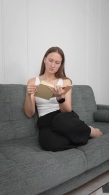 Rahat bir kadın rahat koltukta otururken kitap okuyor, pozisyonlarını değiştiriyor ve sakin boş zamanlarında yüz ifadeleri sergiliyor.