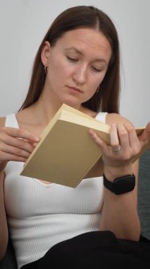 Rahat bir kadın rahat koltukta otururken kitap okuyor, pozisyonlarını değiştiriyor ve sakin boş zamanlarında yüz ifadeleri sergiliyor.