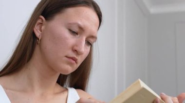 Kanepede oturmuş boş zamanlarının tadını çıkarırken gülümseyen neşeli bir kadın kitap okuyor.,