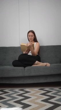 Genç bir kadın kendini kitap okumaya, koltukta rahatça oturmaya, sakin bir ev hayatı yaşamaya ve kişisel rahatlama dikey video görüntülerine kaptırıyor.