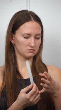 Genç bir kadın evde dinleniyor, doğal tırnaklarını dikkatlice törpülüyor ve şekillendiriyor rahat gri koltukta oturuyor, kişisel güzelliğini ve sağlığını gözler önüne seriyor.