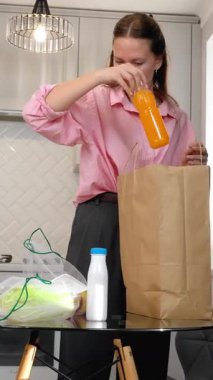 Genç kadın, kese kağıdından yeni alınmış paketleri dikkatlice açıyor. Parlak, modern mutfak alanı dikey video kasetindeki cam sehpanın üzerinde düzenli olarak eşyalar düzenliyor.