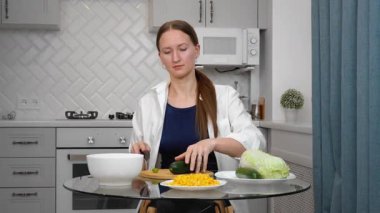 Genç, güzel bir kadın besleyici yemekler pişiriyor, zarif modern mutfağın şeffaf cam masasında renkli sebzeler kesiyor, sağlıklı yaşam tarzı iş salatasına taze bir yaklaşımı somutlaştırıyor..