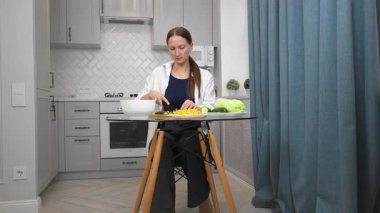 Genç, güzel bir kadın besleyici yemekler pişiriyor, zarif modern mutfağın şeffaf cam masasında renkli sebzeler kesiyor, sağlıklı yaşam tarzı iş salatasına taze bir yaklaşımı somutlaştırıyor..
