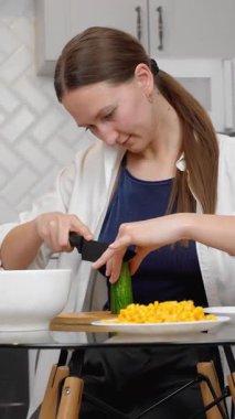 Genç ve güzel bir kadın besleyici yemekler pişiriyor zarif modern mutfağın şeffaf cam masasında renkli sebzeler kesiyor sağlıklı yaşam tarzı iş salatasına taze bir yaklaşımı somutlaştırıyor. dikey video