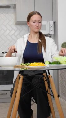 Genç ve güzel bir kadın besleyici yemekler pişiriyor zarif modern mutfağın şeffaf cam masasında renkli sebzeler kesiyor sağlıklı yaşam tarzı iş salatasına taze bir yaklaşımı somutlaştırıyor. dikey video