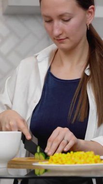 Genç ve güzel bir kadın besleyici yemekler pişiriyor zarif modern mutfağın şeffaf cam masasında renkli sebzeler kesiyor sağlıklı yaşam tarzı iş salatasına taze bir yaklaşımı somutlaştırıyor. dikey video