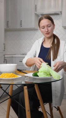 Kadın salata hazırlıyor, sebze kesiyor, mutfaktaki ahşap bir tahtanın üzerinde salatalık kesiyor, mutfak becerilerini ön plana çıkarıyor. dikey video