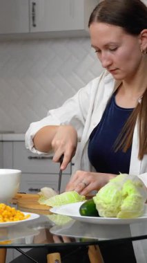 Kadın salata hazırlıyor, sebze doğruyor, mutfakta ahşap bir tahtanın üzerinde Çin lahanası kesiyor, aşçılık becerilerini ön plana çıkarıyor. dikey video
