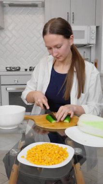 Kadın salata hazırlıyor, sebze kesiyor, mutfaktaki ahşap bir tahtanın üzerinde salatalık kesiyor, mutfak becerilerini ön plana çıkarıyor. dikey video