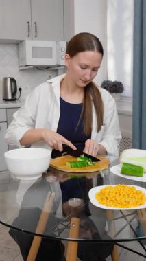 Kadın salata hazırlıyor, sebze kesiyor, mutfaktaki ahşap bir tahtanın üzerinde salatalık kesiyor, mutfak becerilerini ön plana çıkarıyor. dikey video