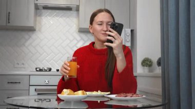 Mutfak masasında taze salata yiyen mutlu güzel bir kadın ve akıllı telefondan sağlıklı yemek yerken mesaj göndermek için uygulama kullanıyor.