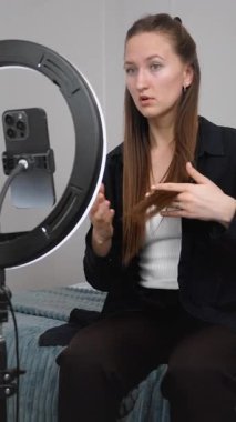 Genç kadın nüfuzlu kişi video blogu kaydederken içerik yaratıyor, profesyonel aydınlatma için halka ışığını kullanıyor ve ev ortamından sosyal medya takipçilerini meşgul ediyor. dikey video