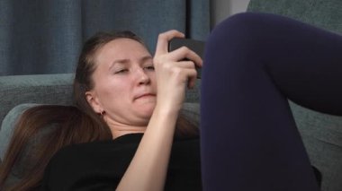 Rahat genç bir kadın, rahat bir şekilde oturma odasındaki kanepeye uzanmış, boş zamanlarında duygusal tepkilerini sergiliyor.