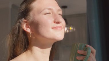 Genç, dingin bir kadın yeşil bardaktan kahve ya da çay içiyor ve pencereden dışarı bakıyor. Güneşin doğuşunun keyfini çıkarıyor ve kahve molası veriyor..