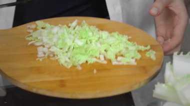 Profesyonel şef, ahşap kesim tahtasıyla taze Napa lahanasını ince ince doğruyor, keskin bıçakla yeşil sebzeleri dilimliyor ve yemek hazırlıkları sırasında doğranmış lahanayı beyaz kaseye aktarıyor.