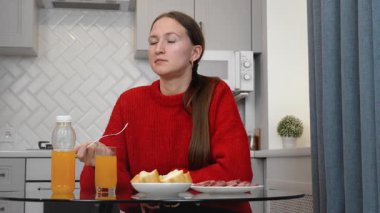 Sağlıklı sosis ve salatanın tadını çıkaran genç bir kadın. Parlak, modern bir mutfakta cam masada oturmuş besleyici yemeğin tadını çıkarırken içeriğini dile getiriyor.