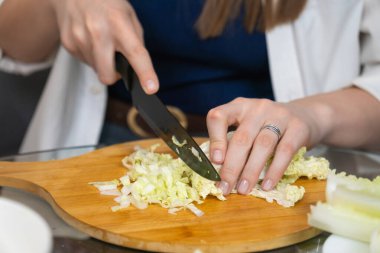 Ahşap kesim tahtasında taze Pekin lahanası dilimleyen kadın şef, profesyonel bir mutfak ortamında sağlıklı bir yemek için gerekli malzemeleri hazırlıyor.