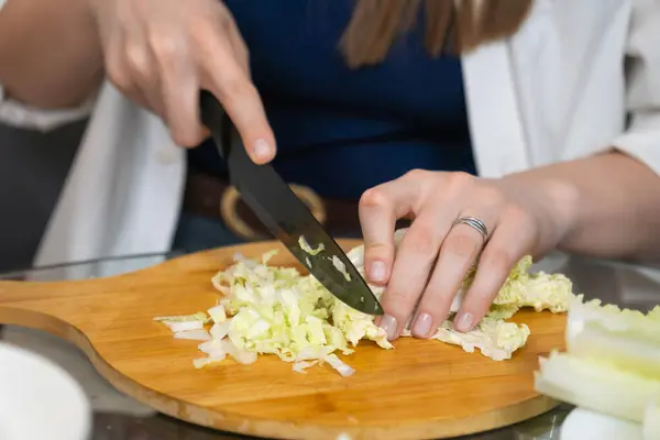 Ahşap kesim tahtasında taze Pekin lahanası dilimleyen kadın şef, profesyonel bir mutfak ortamında sağlıklı bir yemek için gerekli malzemeleri hazırlıyor.