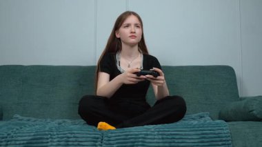 Genç kız oturma odasındaki rahat koltukta bacak bacak üstüne atarak bilgisayar oyunu oynamaktan hoşlanıyor. Ekranda olanlara odaklanıyor.