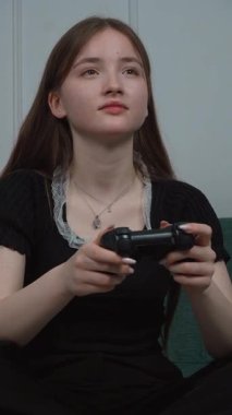 Genç kız oturma odasındaki rahat koltukta bacak bacak üstüne atarak bilgisayar oyunu oynamaktan hoşlanıyor. Ekranda olanlara odaklanıyor.