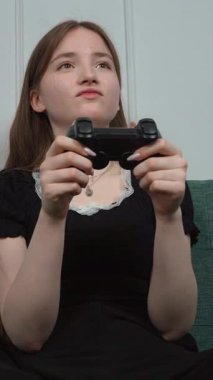 Kız Oyuncu Rahat Ev Ortamı dikey videosundaki video oyununun tadını çıkarırken Kanepede bacak bacak bacak üstüne atarak Kablosuz Oyun Kontrolörü