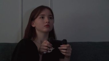 Genç kız kanepede bağdaş kurup video oyunları oynuyor. Yoğun duygusal tepkiler gösteriyor. Yoğunlaştırılmış konsantrasyonla dijital oyun oynuyor.