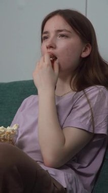 Kanepesinde rahat bir şekilde, genç bir kadın nişanlı bir film izlerken bir kase patlamış mısırın keyfini çıkarıyor. İfadeleri anlatılan hikayenin dikey videosuyla değişiyor.