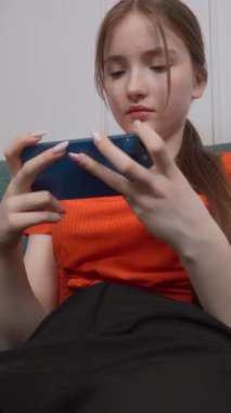 Genç kız rahat ev koltuğunda dinleniyor, akıllı telefon elinde, sosyal medyada geziniyor ya da kayıtsız, kaygısız video oyunu oynuyor.